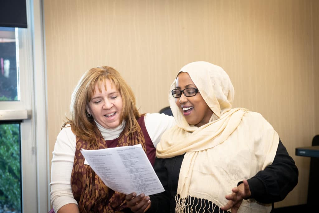 two women, one in hijab, sharing a song sheet