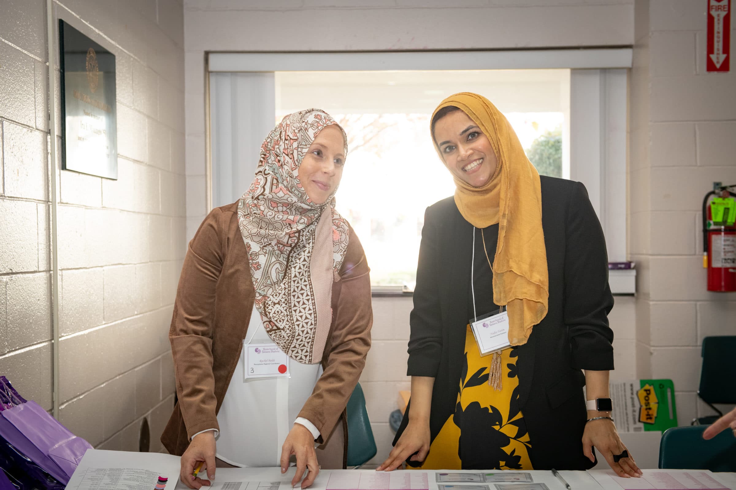 two women in hijab standing at table in smiling