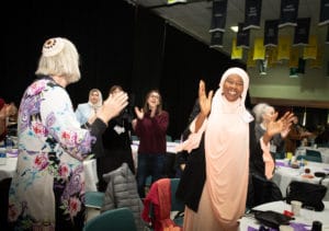 Muslim woman in hijab clapping, surrounded by other clapping women