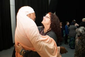 Muslim woman in hijab hugs woman with curly hair and glasses