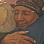 gray haired woman in kipper and African American woman in headscarf embrace
