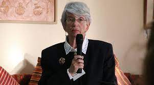 grey haired woman in black suit holding a microphone
